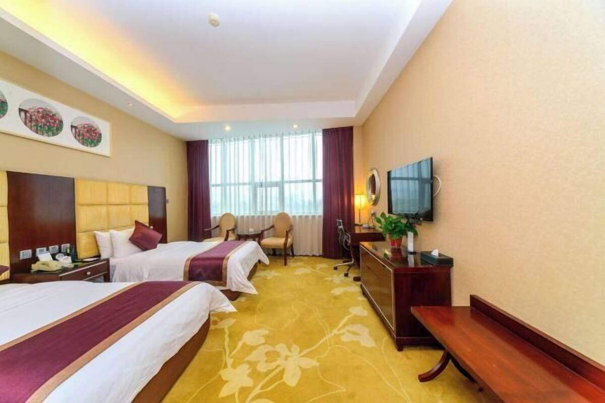 Une chambre d’hôtel avec deux lits, un bureau, une chaise, une télévision et une fenêtre avec des rideaux.