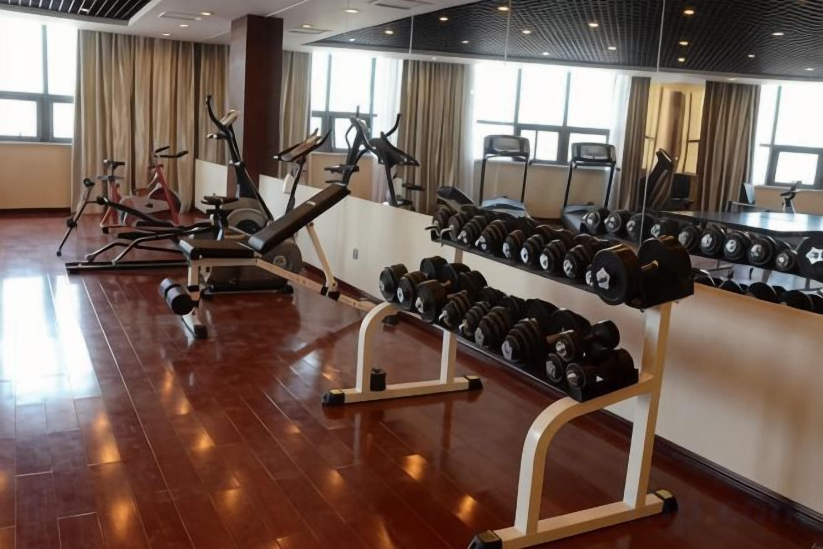 A gym with cardio machines, dumbbells, and a mirror wall.