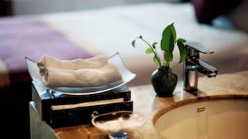 A bathroom with a marble sink, a glass bowl with towels, a potted plant, and a modern faucet.