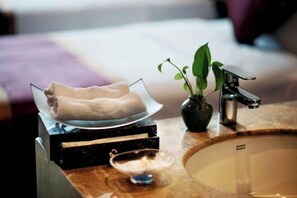 A bathroom with a marble sink, a glass bowl with towels, a potted plant, and a modern faucet.