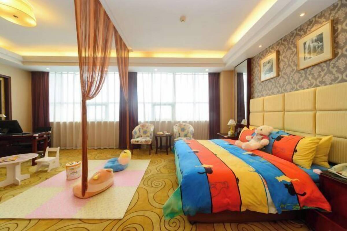 Une chambre d’hôtel avec un grand lit, un coin salon avec une table et des chaises, une grande fenêtre et un rideau.