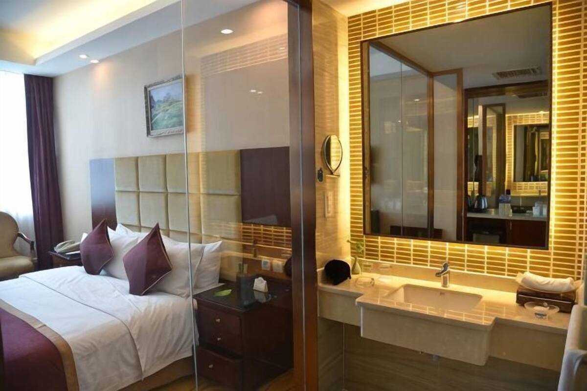 Une chambre d’hôtel comprenant un lit, une table de chevet, un miroir et une salle de bain avec un lavabo et un miroir.