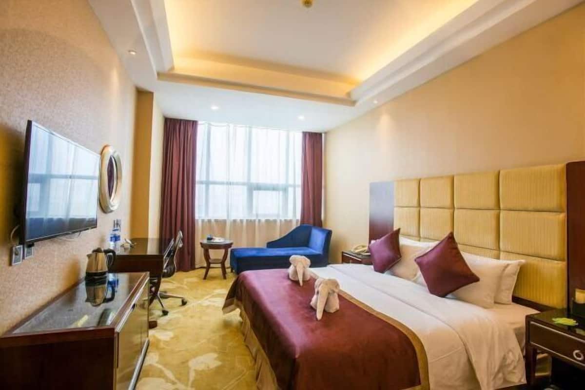 Une chambre d’hôtel avec un grand lit, un bureau doté d’un téléviseur à écran plat, une chaise et une fenêtre avec des rideaux.