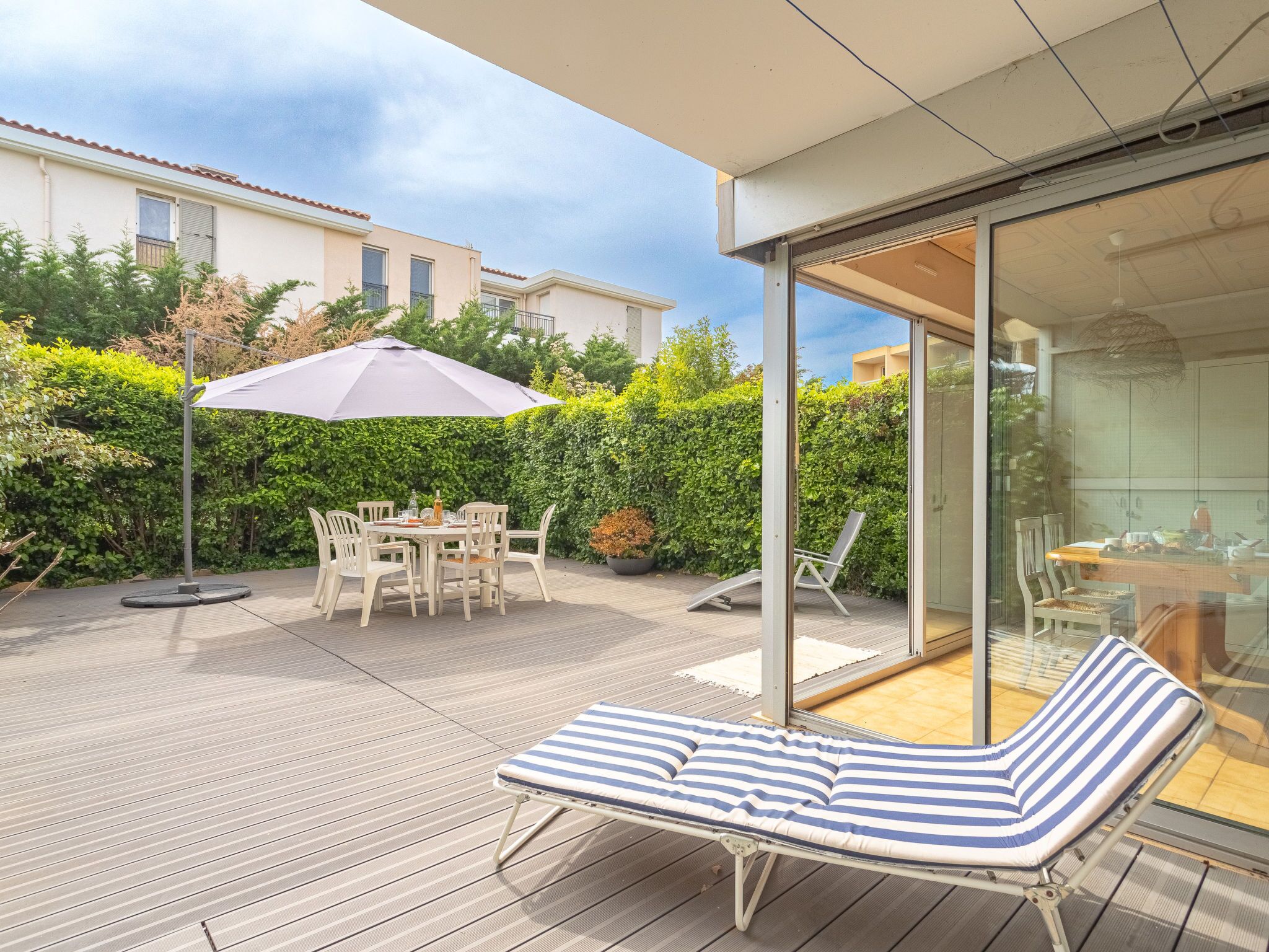 A modern outdoor patio with a dining table, chairs, a lounge chair, and a large umbrella.