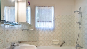 Un baño con lavamanos, espejo, ducha y azulejos estampados.