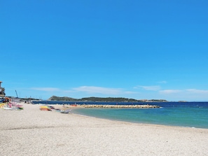 En strand med sten, en klippefyldt mole og klart, blåt vand.