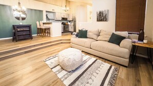 A modern living room with a beige sofa, a coffee table, and a rug. There is a kitchen in the background with a dining area. - Cozy Lakeview Condo - 60 Day Special (Littleton)