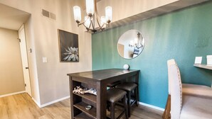 A dining area with a dark wooden table, two chairs, a chandelier, a round mirror, and a teal accent wall. - Cozy Lakeview Condo - 60 Day Special (Littleton)