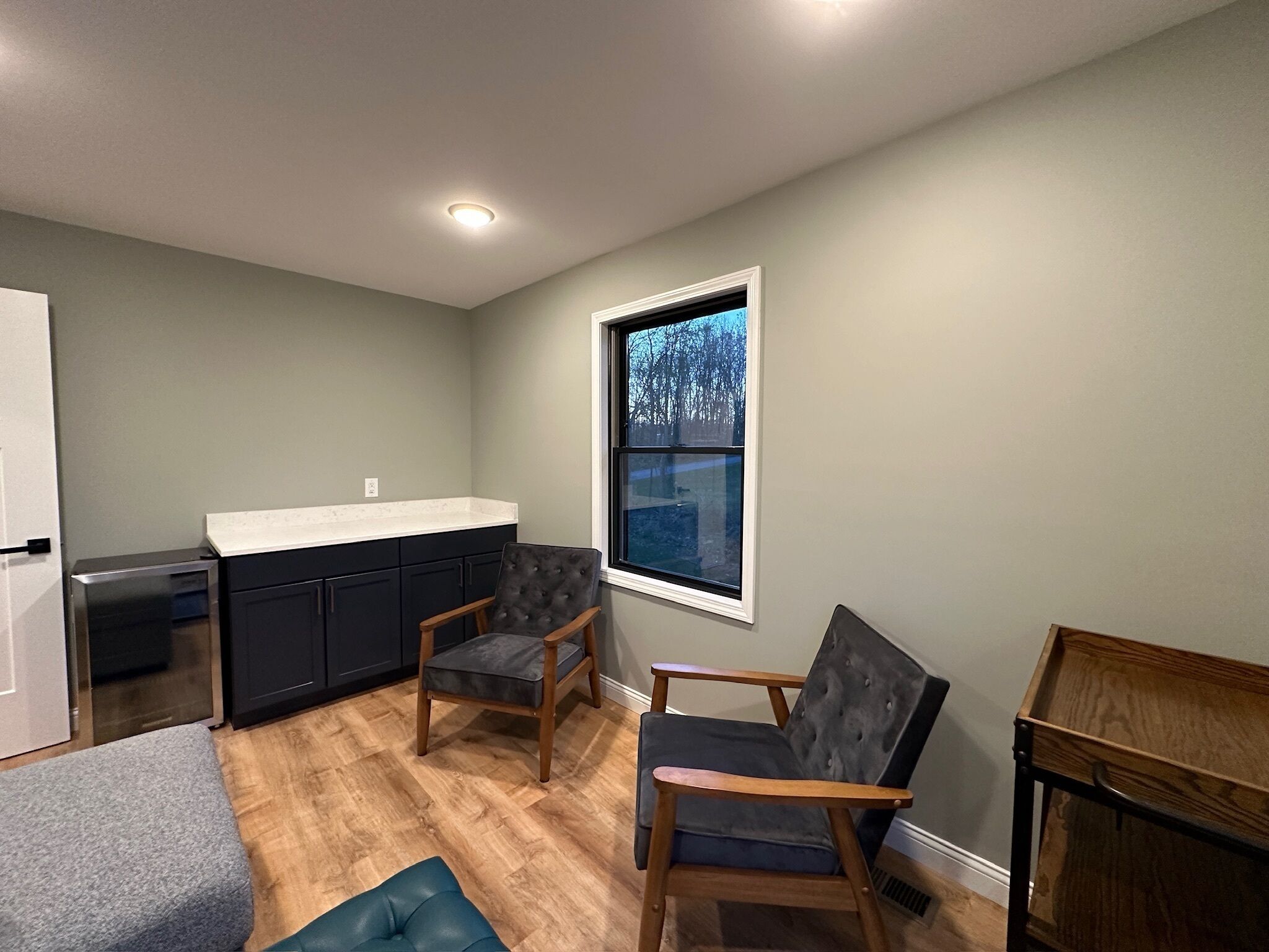 A compact kitchen with dark cabinets, a white countertop, and a window with a view of trees.