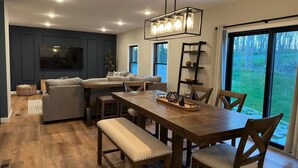 Una sala moderna con una mesa de comedor de madera, asientos acolchados y un televisor grande.