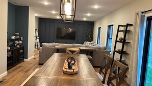 Una sala de estar moderna con una mesa de comedor de madera, sofás grises y un televisor montado en la pared.