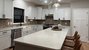Una cocina moderna con armarios blancos, un salpicadero de ladrillo y una isla central con asientos.
