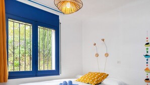 Un dormitorio con cama, cortinas azules, una ventana con barrotes y un adorno en la pared.