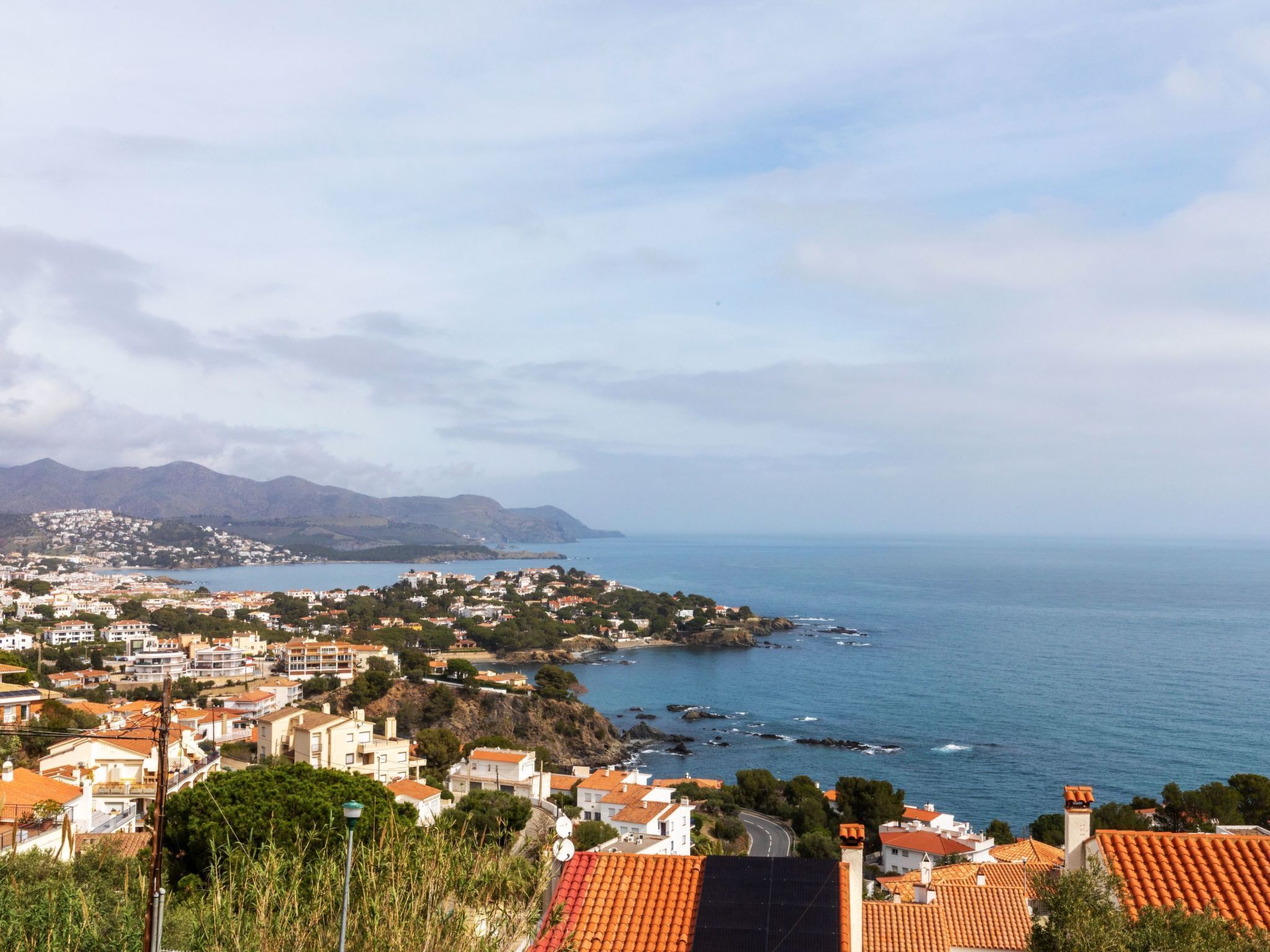 Une ville côtière aux bâtiments aux toits de tuiles rouges, offrant une vue dégagée sur la mer et bordée de montagnes en arrière-plan.
