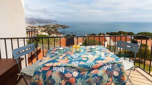 Un balcón con una mesa lista para dos personas, con vista a un pueblo costero y al mar.