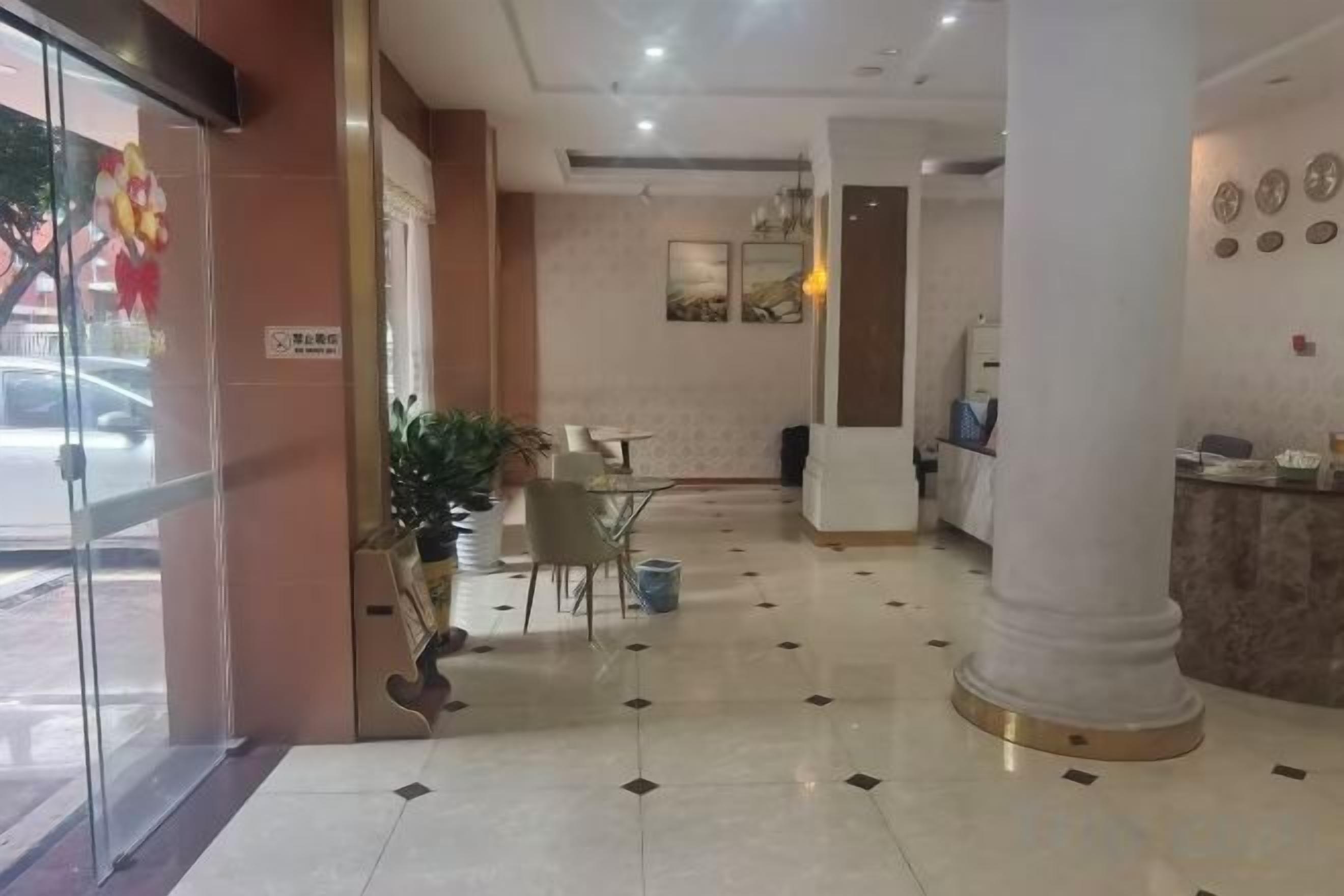 A hotel lobby with a reception desk, seating area, and a glass door entrance.