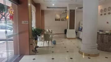 A hotel lobby with a reception desk, seating area, and a glass door entrance.