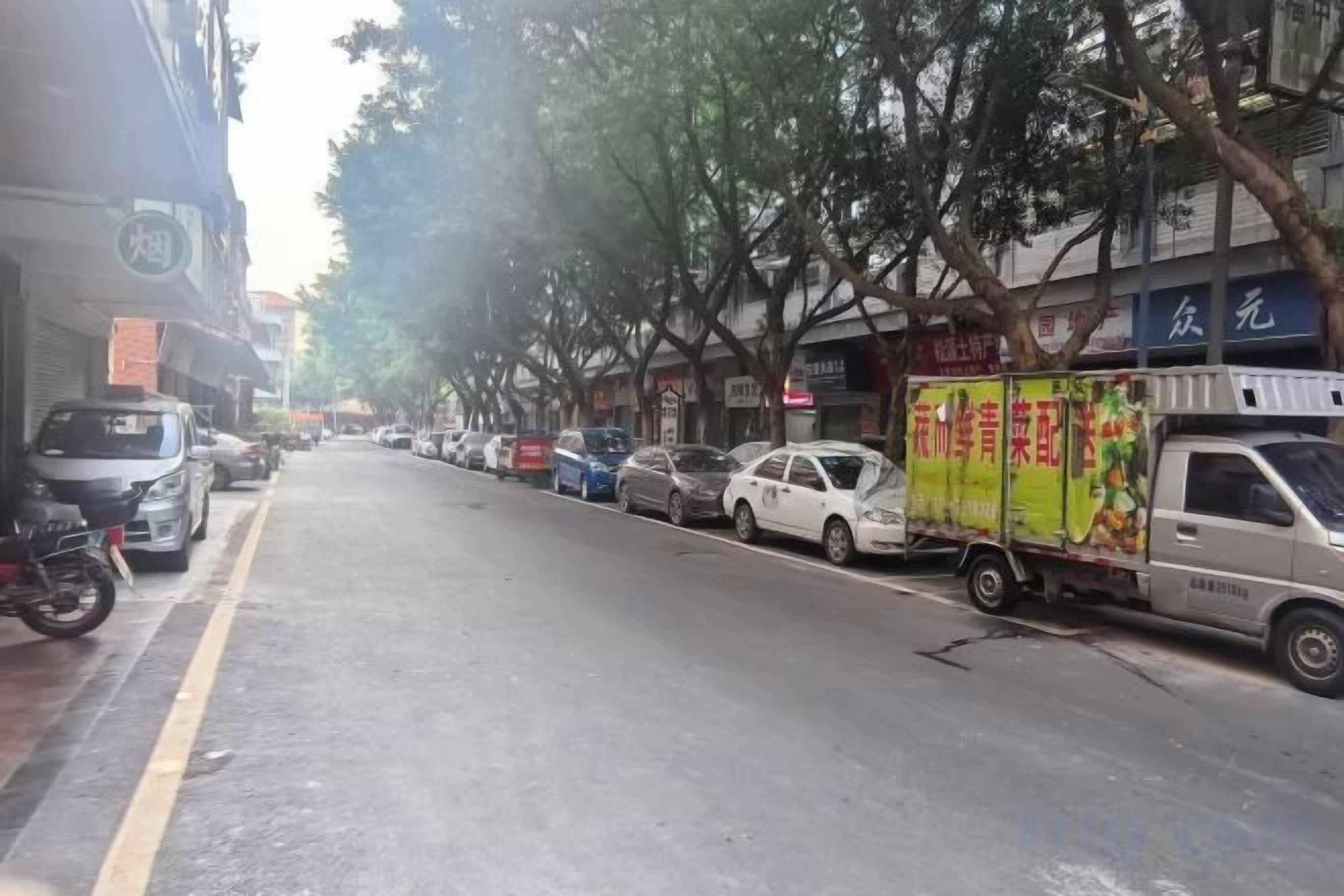 Una calle con automóviles estacionados y un camión de reparto a la derecha.