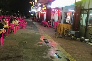 Un área de comedor al aire libre con sillas y mesas rosas, un sendero pavimentado y un edificio con señalización.