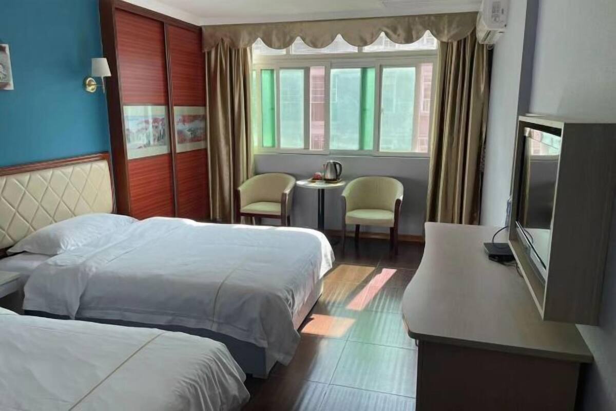 Una habitación de hotel con dos camas, una mesita con sillas, televisión y ventana con cortinas.