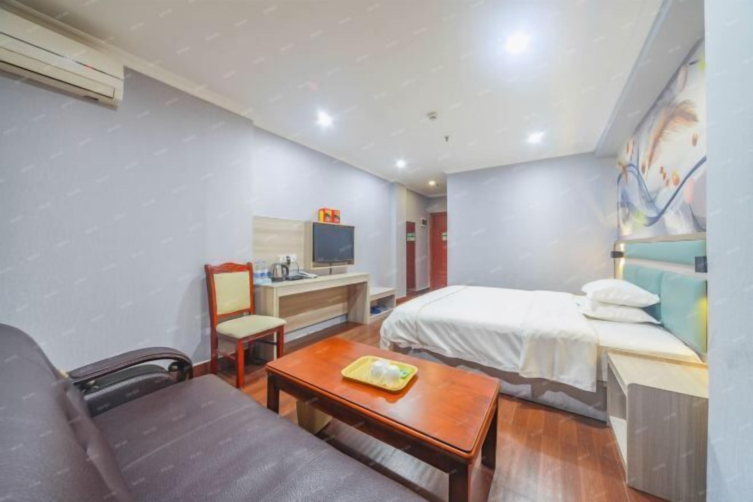 Habitación de hotel con cama, escritorio con computadora, silla, mesa con bandeja y equipo de aire acondicionado.
