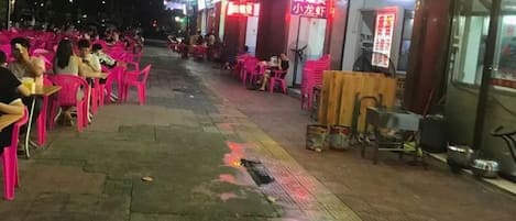 An outdoor seating area with tables and chairs, a wet ground, and a storefront with signage.