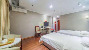 A hotel room with a bed, a desk with a chair, an air conditioner, and a television.