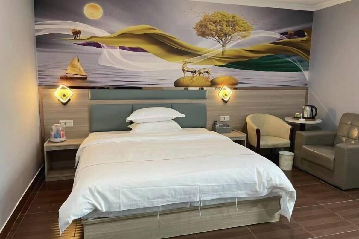Una habitación de hotel con cama, mesita de noche, silla y un mural en la pared.