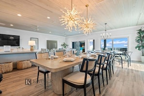 A spacious dining area with a large wooden table, multiple chairs, and a modern chandelier.