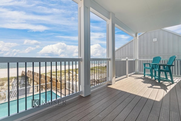 Una terraza de madera con piscina, vista a la playa y dos sillas.