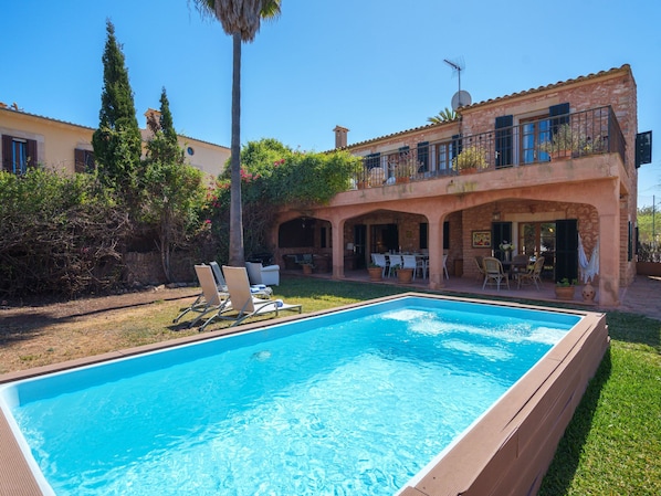 Una casa de dos pisos amb piscina, zona de seients a l'exterior i jardí.