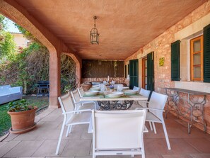 Terrassa exterior amb taula preparada per a dinar, envoltada de caires blancs i una paret de pedra.