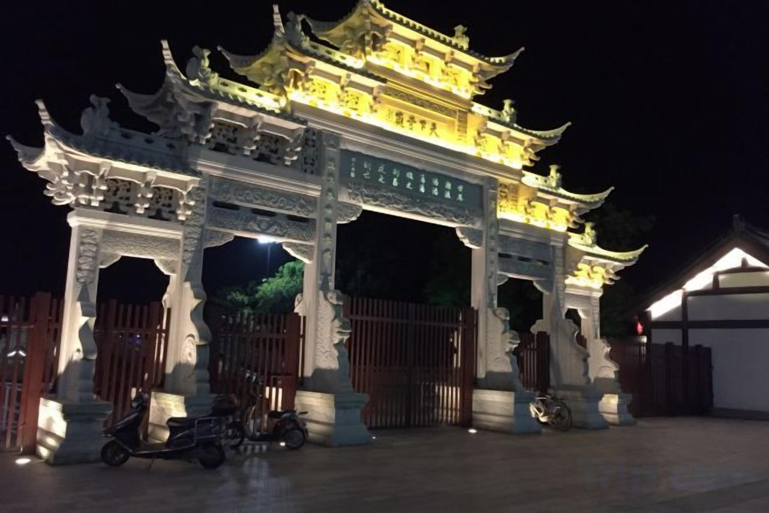 Ein traditionelles chinesisches Tor mit aufwendigen Schnitzereien und einem goldenen Dach, beleuchtet bei Nacht.