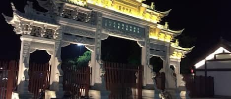 A traditional Chinese gate with intricate carvings and a golden roof, illuminated at night.