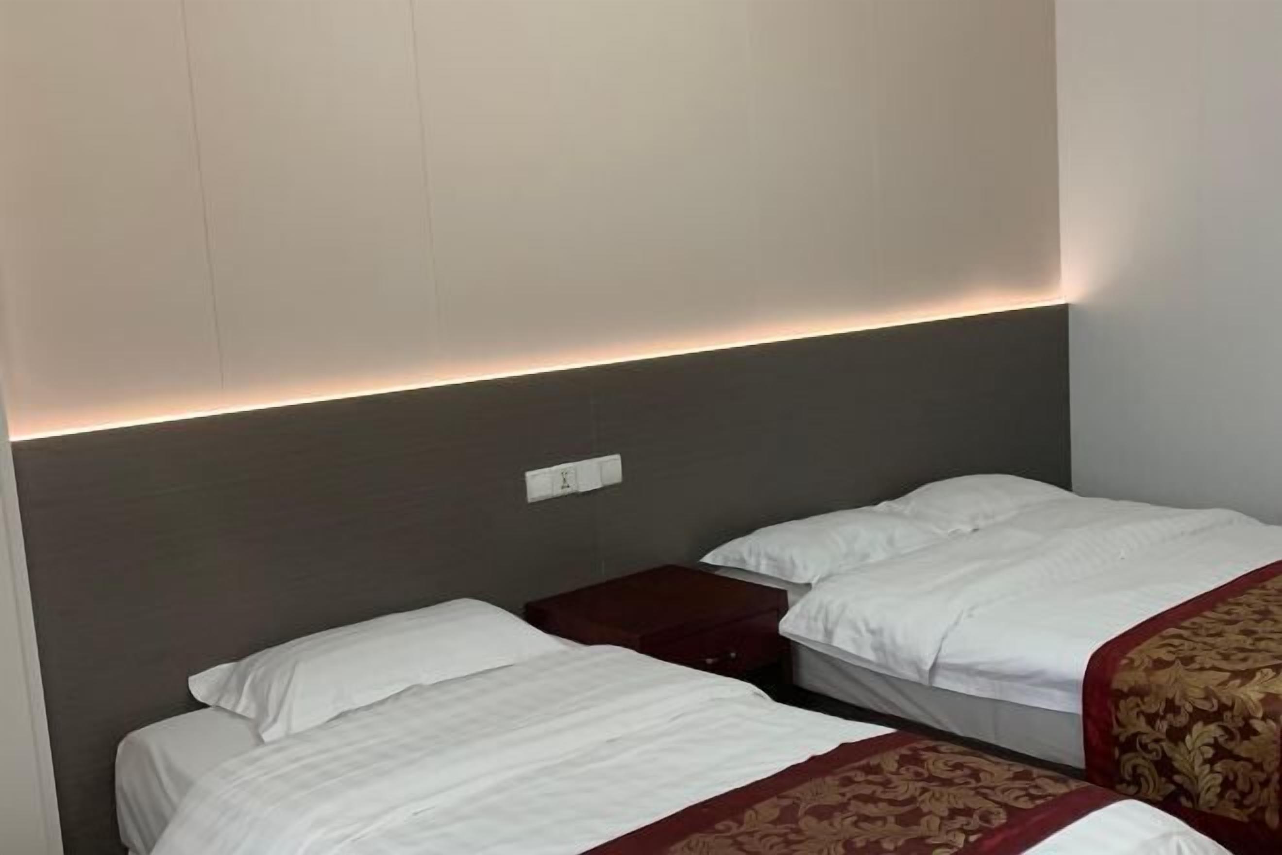A hotel room with two beds, a dark headboard, a bedside table, and a wall socket.