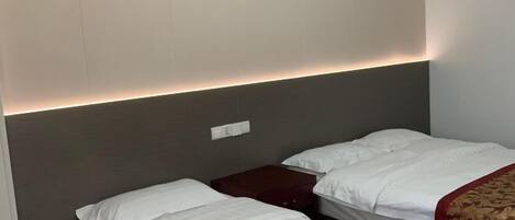 A hotel room with two beds, a dark headboard, a bedside table, and a wall socket.