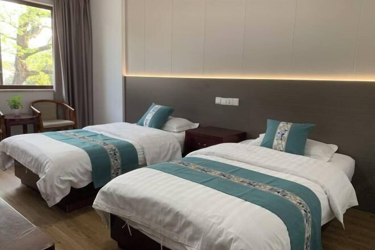 Habitación de hotel con dos camas, una mesita, una silla y una ventana con cortinas.
