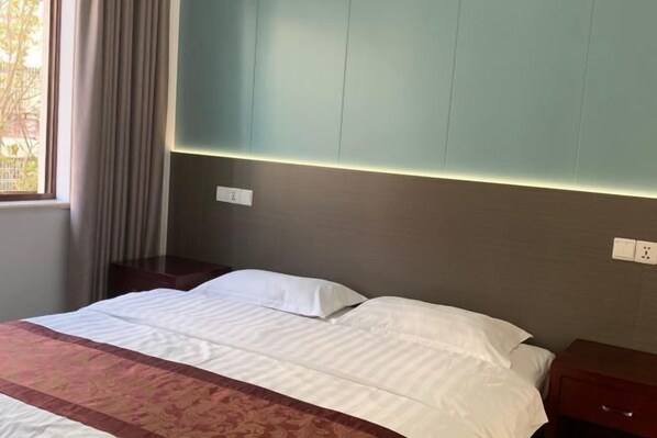 Habitación de hotel con cama, mesita de noche, toma de corriente y ventana con cortinas.