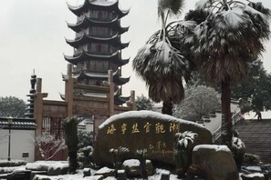 A traditional pagoda-style building with a multi-tiered roof, surrounded by snow-covered rocks and palm trees. - Haining chunxi hotel (Haining)