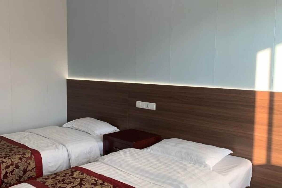 A hotel room with two beds, a wooden headboard, a nightstand, and a wall-mounted light.