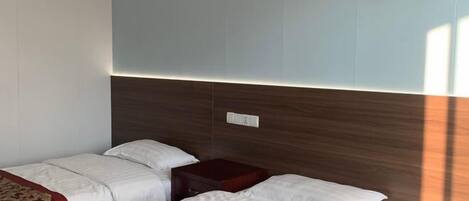 Une chambre d’hôtel avec deux lits, une tête de lit en bois, une table de chevet et une lampe fixée au mur.