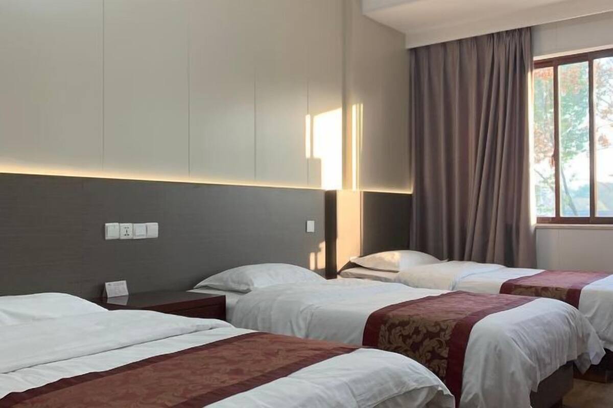 Habitación de hotel con tres camas, un ventanal con cortinas y una lámpara fijada a la pared.