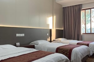 Habitación de hotel con tres camas, un ventanal con cortinas y una lámpara fijada a la pared.