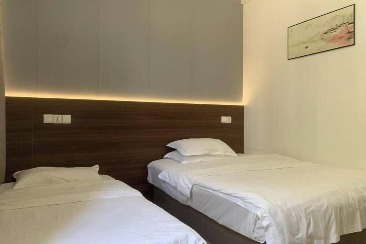 Habitación de hotel con dos camas individuales, cabecero de madera, luz de pared y una obra de arte enmarcada.