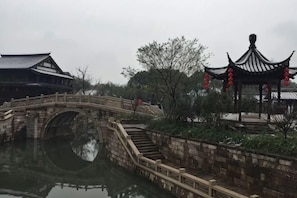 Un jardín chino tradicional con un puente de piedra, un pabellón y un edificio con tejado de cerámica.