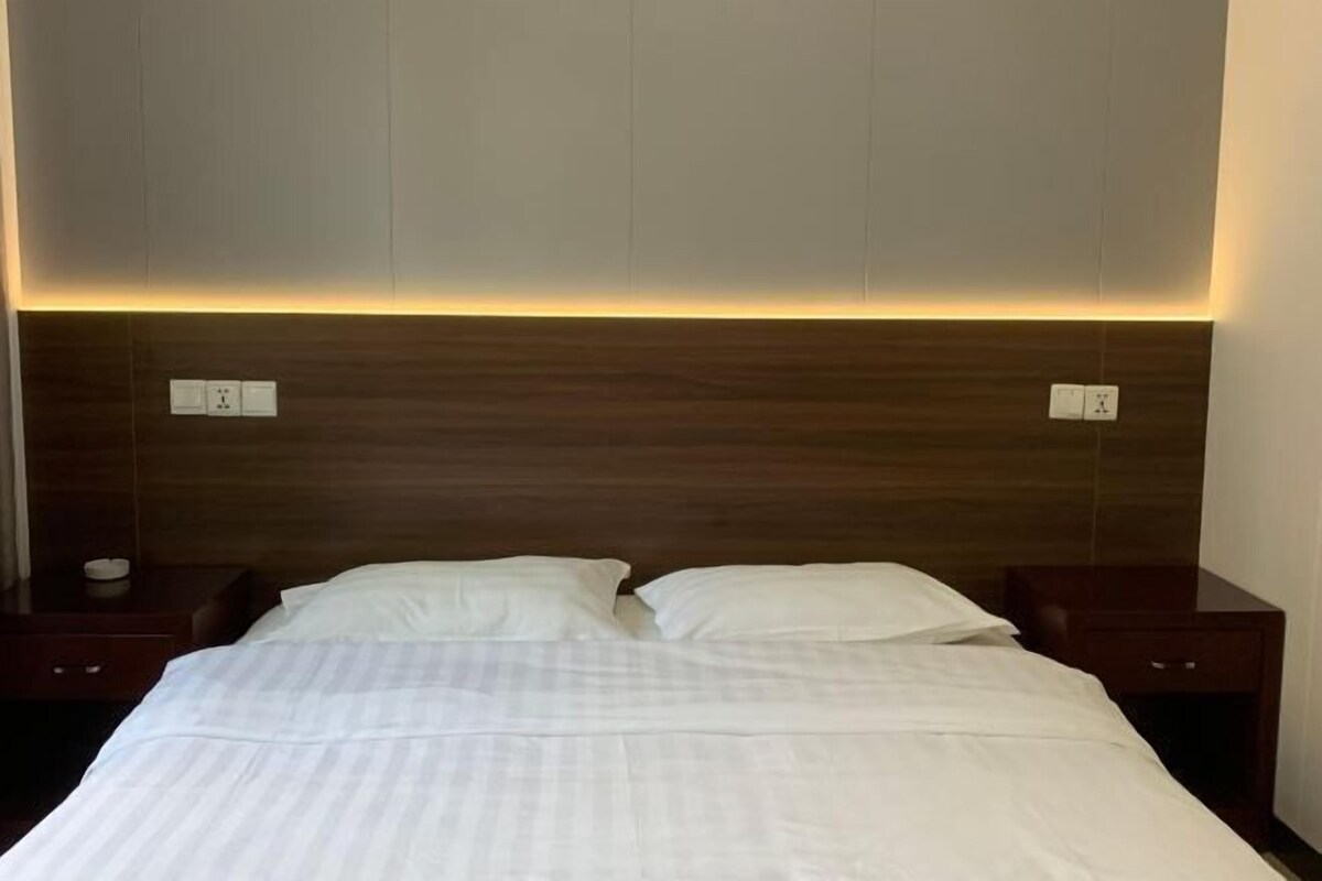 A hotel room with a large bed, two bedside tables, and a wooden headboard with built-in lighting.