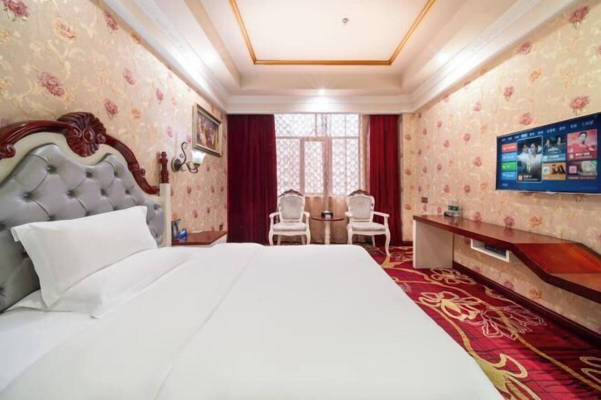 A hotel room with a large bed, a television, a desk, and a window with curtains.