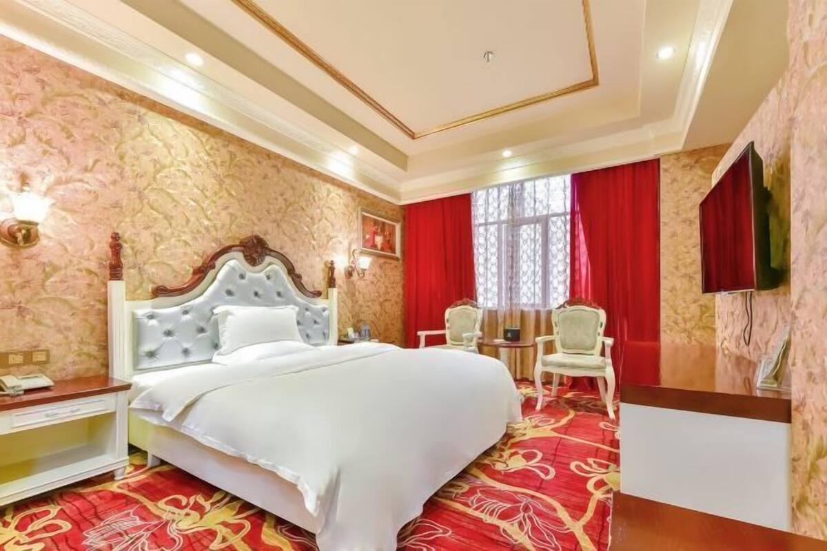 A hotel room with a large bed, a desk, and two chairs.