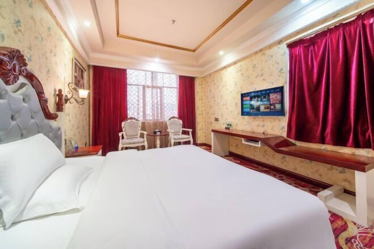 A hotel room with a large bed, a desk, two chairs, and a television.