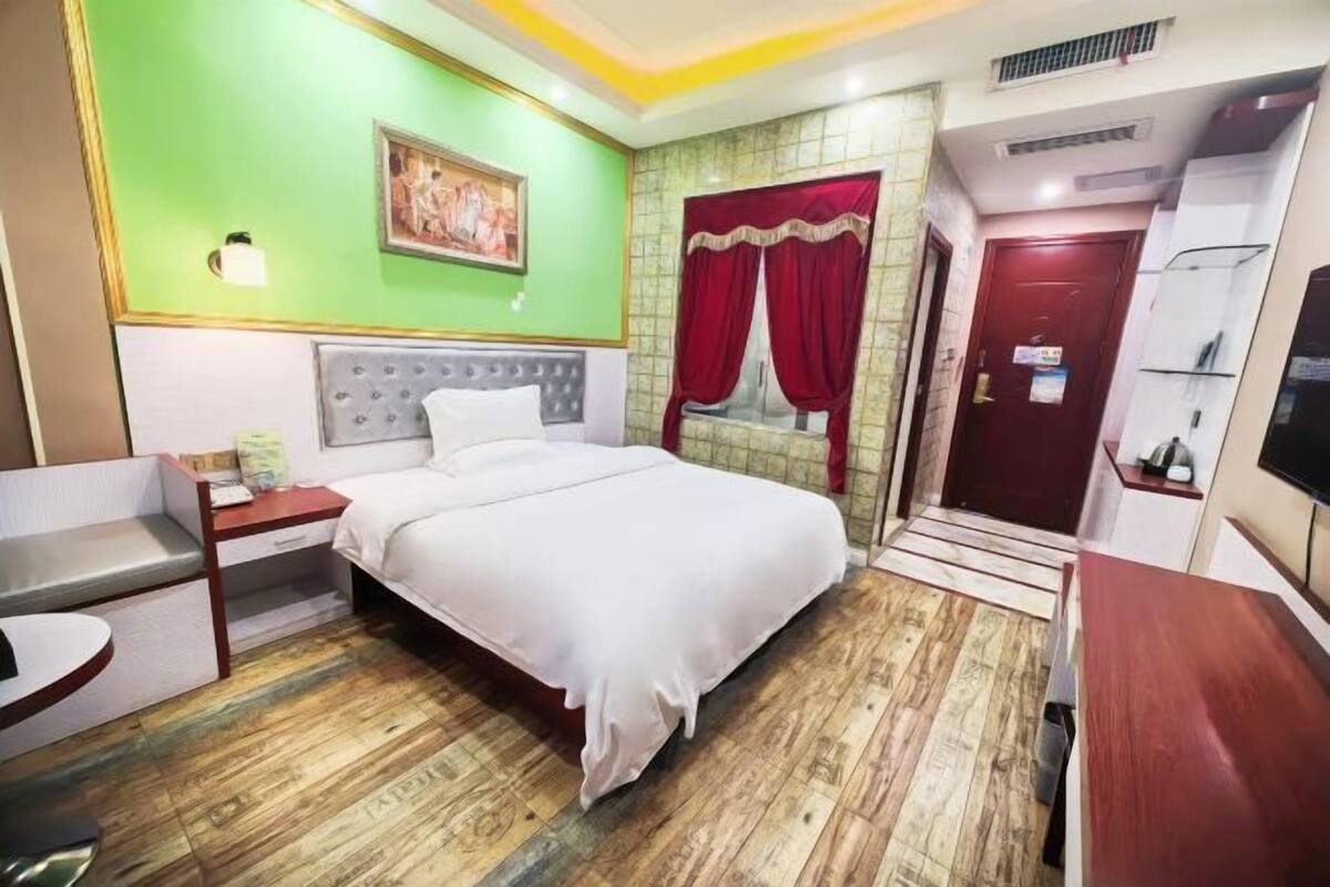 A hotel room with a bed, bedside table, chair, and a TV.